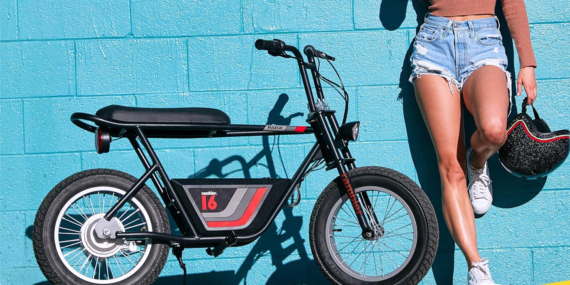 Razor Rambler 16 electric minibike standing next to woman against bright blue wall, within post for Snapcycle R1 Pro e-bike