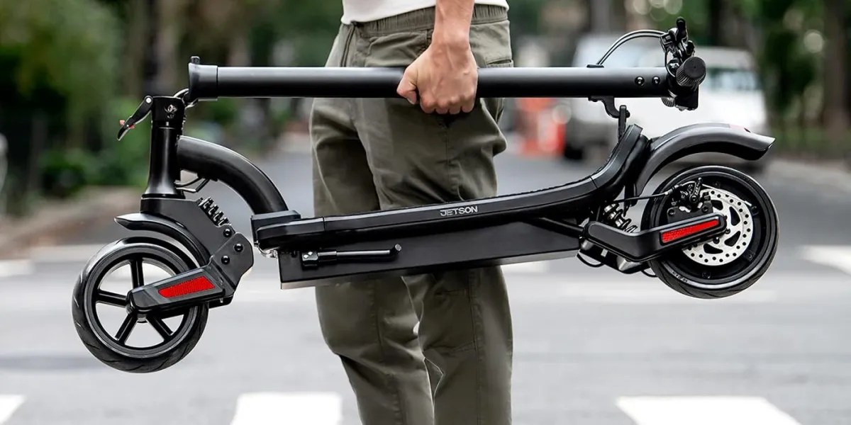 man holding a folded up Jetson Canyon electric kickscooter in a crosswalk. Picture is within post for the Lectric XPress Commuter e-bikes