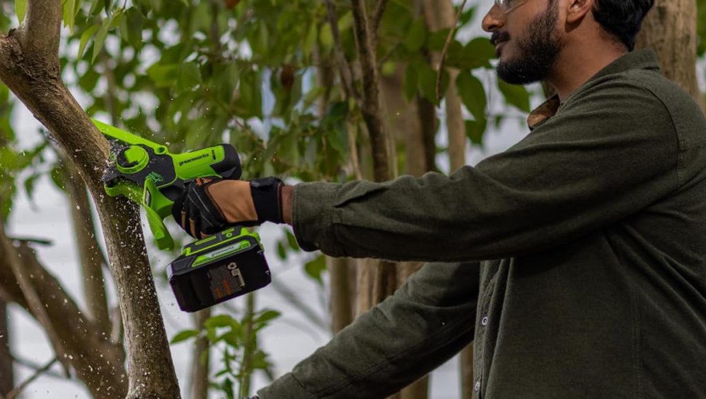 man using Greenworks 24V 6-inch cordless electric mini chainsaw on tree branch