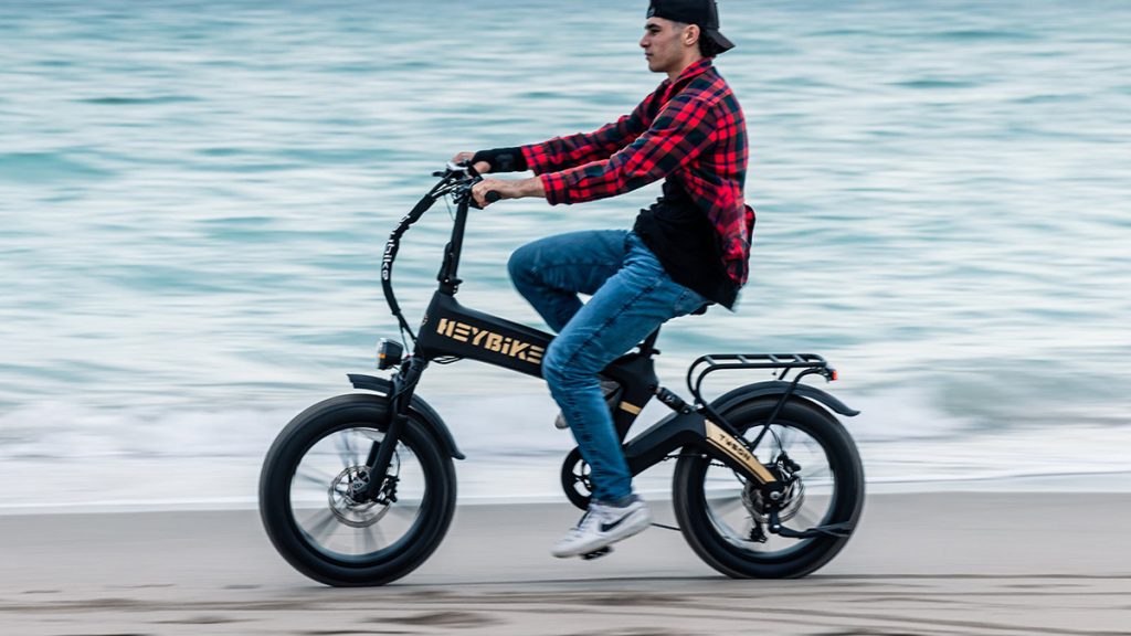 man riding heybike tyson e-bike down beach near water