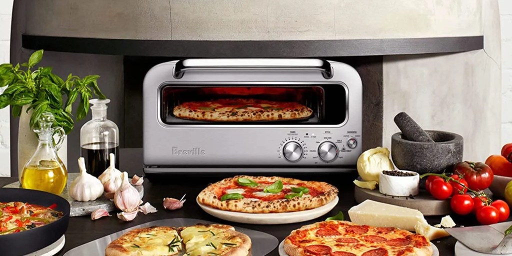breville pizza oven on countertop with pizzas, tomatoes, cheese, and more