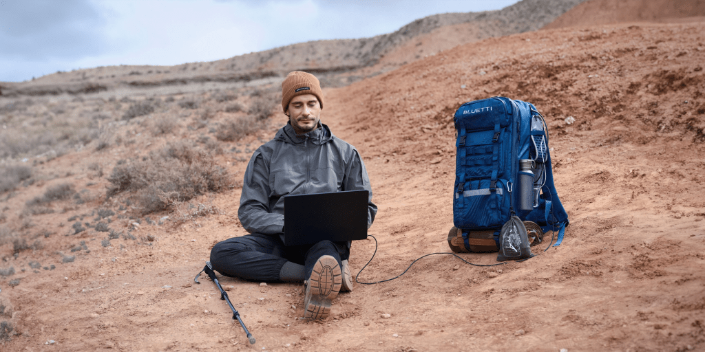 man using Bluetti Handsfree 1 backpack power station to run laptop in desert