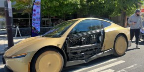 Gold Tesla Cybercab stopped on South Broad Street in Philadelphia with the outer panel of its driver-side door missing